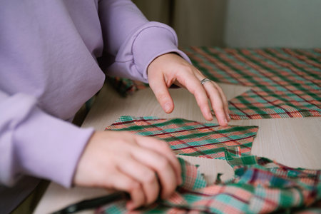 Closeup of female tailor cuting out checkered fabric with a paper pattern to make out a shirt