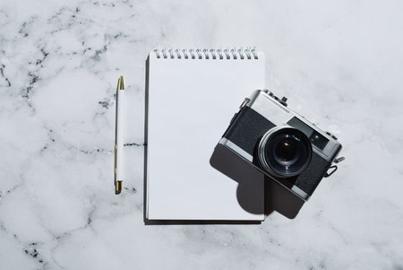 Flatlay of vintage film camera and notebook with pen on marbleの写真素材