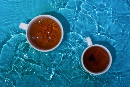 Two cups of tea in blue splashing waterの写真素材