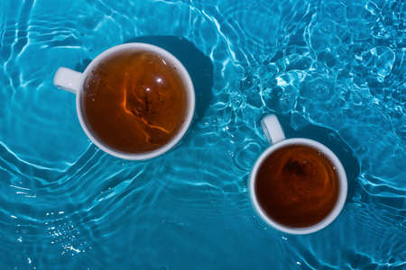 Two cups of tea in blue splashing waterの写真素材