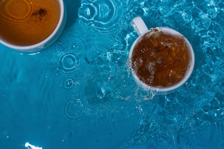 Two cups of tea in blue splashing waterの写真素材