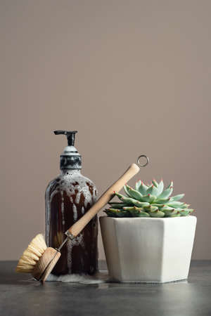 Eco-friendly amber glass soap bottle, wooden dish brush and succulent on dark marble background, sustainable homecare conceptの写真素材