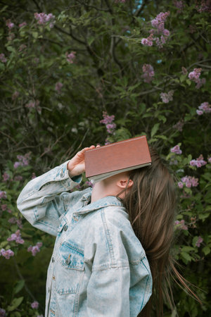 Faceless shot of female holding a book in front of her face outdoors,の写真素材