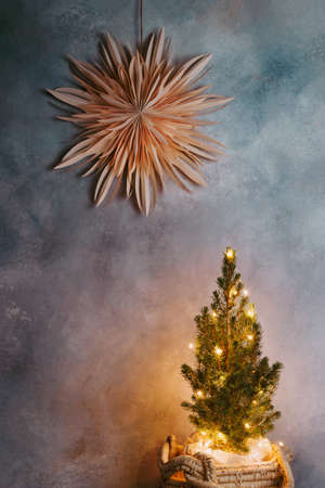 Paper star ornament on the wall and Christmas tree decorated with lights, minimalist festive decorationsの写真素材