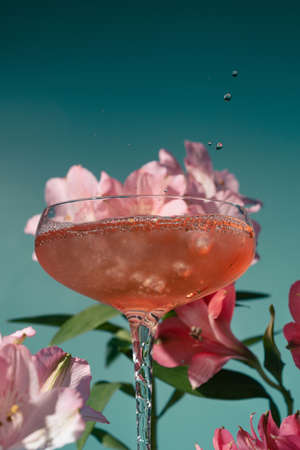 Closeup of wine or cocktail in a glass surrounded by pink and magenta alstroemeria flowers on blueの写真素材