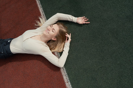 Young smiling blonde female lying on a backetball sport field
