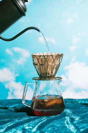 Water pouring into metall dripper with paper filter and iced coffee in front of blue sky, alternative brewingの写真素材