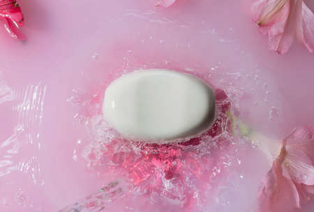 White soap bar in pink splashing water with flowers, body care concept,の写真素材
