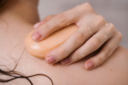 Closeup of female back with her hand on the shoulder with a bar of natural soap,の写真素材