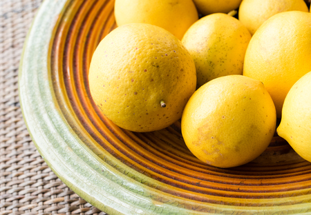 Close up of natural looking lemons on coloured plate on rattan table (cropped and selective focus)の写真素材