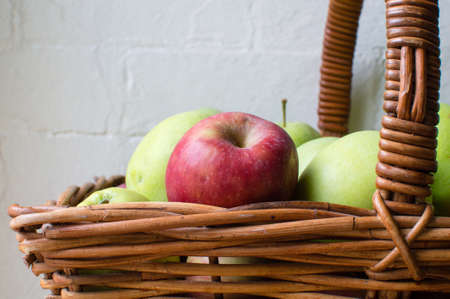 Red apple in a wicker basket of green apples against a white brick wall (close up)の写真素材