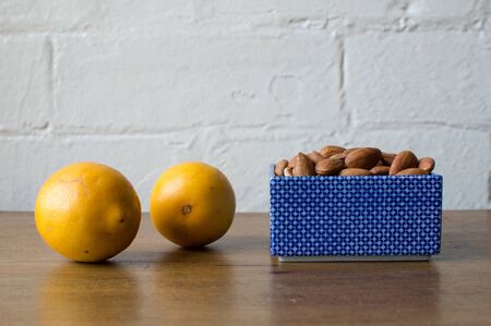 Almonds in a blue dish with two lemons on a wooden table against a white brick wallの写真素材