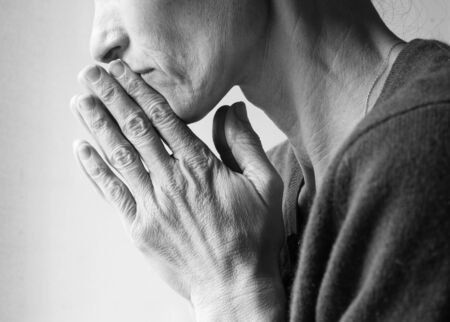 Mature woman in profile with hands clasped in prayer (cropped and black and white)の写真素材