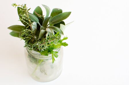 High angle view of small bunch of herbs (parsley, sage, thyme) in glass jar on white tableの写真素材