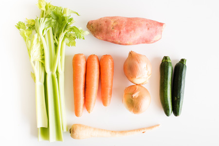 High angle view of celery, carrots, onions, sweet potato, zucchini and parsnip on a white tableの写真素材