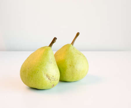 Two green pears on a white table against a neutral backgroundの写真素材