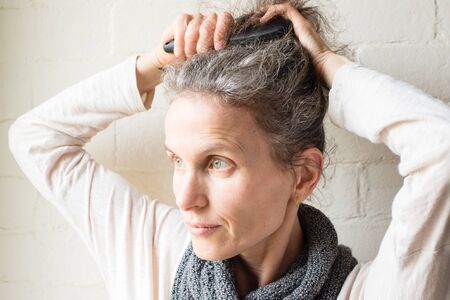 Middle aged woman brushing grey hairの写真素材