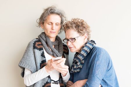 Middle aged daughter and older mother wearing winter scarves and looking at smart phone together