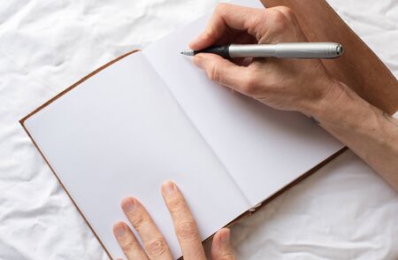 Close up, high angle view of middle aged woman's hands holding pen ready to write in brown leather bound journalの写真素材