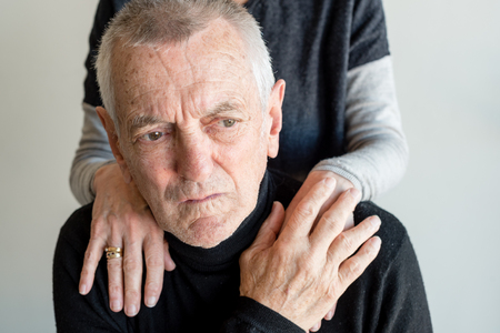 Distressed older man with short grey hair and black top being comforted by older woman (selective focus)の写真素材