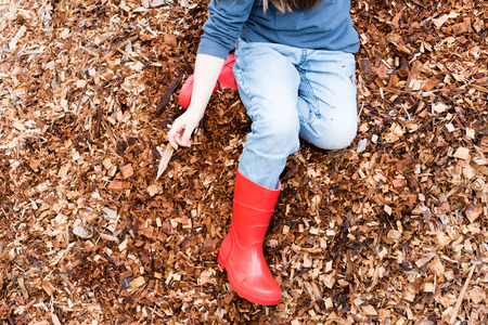High angle view of little girl in blue top, jeans and red boots playing in woodchip pile (cropped)の写真素材