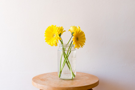 Yellow gerberas in a glass jar on small wooden table (close up)の写真素材