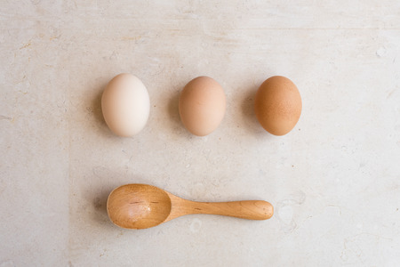 High angle view of white, beige and brown eggs with wooden spoon on natural limestone background