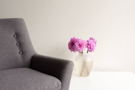 Grey armchair and white table with bright pink dahlias in glass vase (selective focus)の写真素材