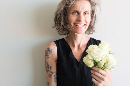 Middle aged woman with grey hair and black top smiling and holding cream roses (selective focus)の写真素材