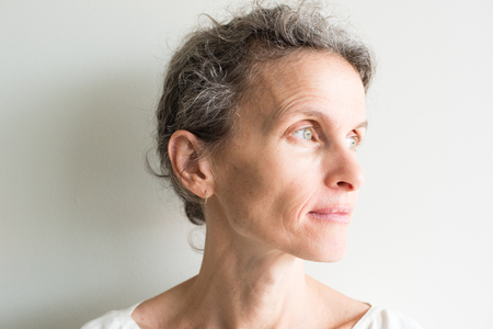 Close up of middle aged woman with grey hair and cream top looking hopeful (cropped and selective focus)の写真素材
