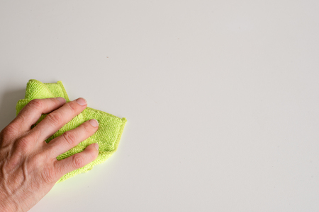 Close up high angle view of woman's hand using green microfibre cleaning cloth on white table...
