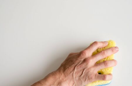 Close up high angle view of woman's hand using yellow cleaning sponge on white table (selective focus)の写真素材