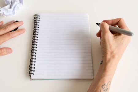 High angle view of middle aged woman's hands holding pen to write in notebook (selective focus)