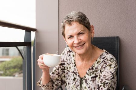 Older woman sitting on balcony, smiling with coffee cup (selective focus)の写真素材