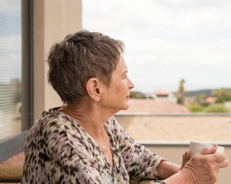 Older woman with short hair holding cup and looking out over balcony (selective focus)