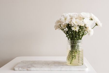White chrysanthemums in glass jar on marble board on white table against neutral background with copy space to leftの写真素材