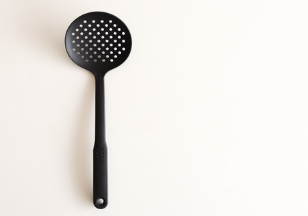 High angle view of round black plastic cooking spatula with holes on white table on copy space to leftの写真素材
