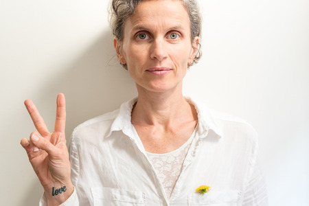 Middle aged woman looking at camera and holding fingers in peace sign (selective focus)の写真素材