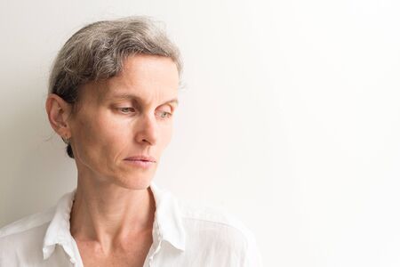 Head and shoulders view of middle aged woman with grey hair looking down sadly (selective focus)の写真素材