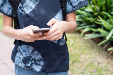 Cropped close up view of teenage boy using smart phone outdoors (selective focus)の写真素材