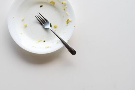 High angle cropped view of dirty white dinner plate with metal fork on white table with copy space...