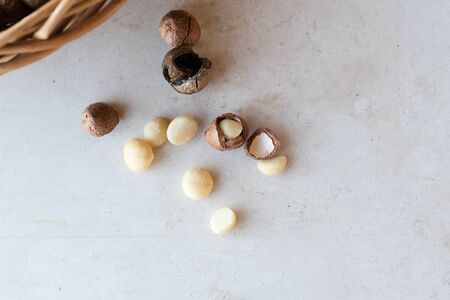 High angle close up view of whole and cracked macadamia nuts on cream limestone background with copyspace and wicker basket at edge of frame (selective focus)の写真素材