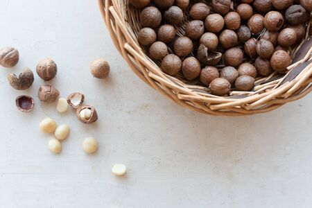 High angle close up view of wicker basket and whole and cracked macadamia nuts scattered on cream limestone background (selective focus)の写真素材