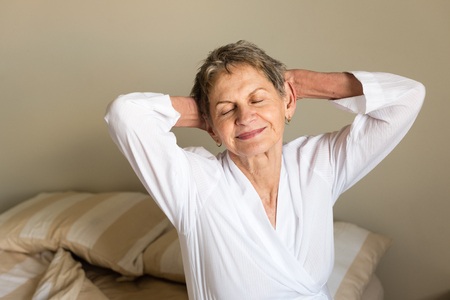 Cropped view of elderly woman in white bathrobe stretching and smiling (selective focus)の写真素材