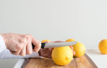Close up of middle aged woman's hand holding knife and preparing to slice lemon on wooden chopping board (selective focus)の写真素材