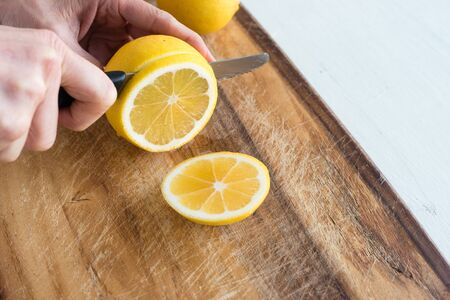 Close up high angle view of middle aged woman's hand slicing lemon on wooden chopping board (selective focus)の写真素材