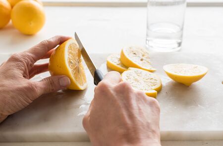 Close up of middle aged woman's hand holding knife and slicing lemon on marble chopping board (selective focus)の写真素材