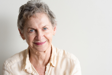 Portrait of beautiful older woman with short grey hair and blue eyes against neutral background...