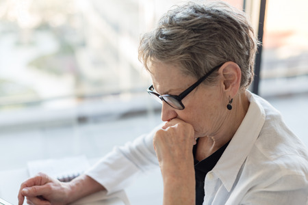 Profile of professional older woman with glasses concentrating at desk (selective focus)の写真素材