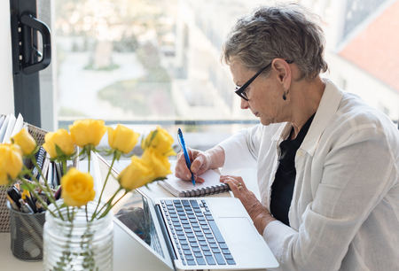 Professional older woman working at desk with computer by a window (selective focus)の写真素材